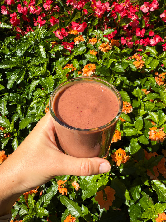 glass cup full of smoothie with orange and red flowers in background